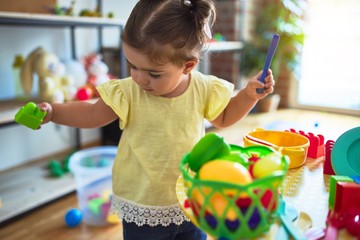 Beautiful toddler playing on the table with plastic vegetables and dishes at kindergarten