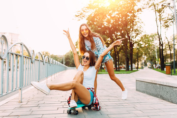 Two stylish excited girls have fun and skateboard in the Park in Sunny weather