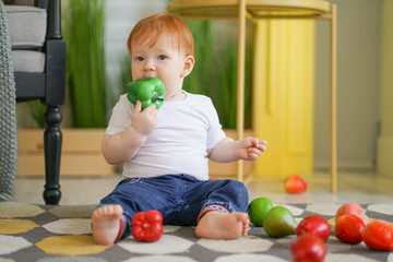 Fototapeta premium chubby child with red hair plays with vegetables
