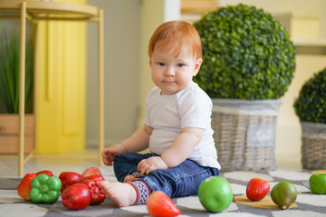 Fototapeta premium chubby child with red hair plays with vegetables