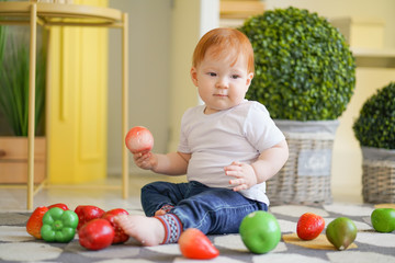 Fototapeta premium chubby child with red hair plays with vegetables