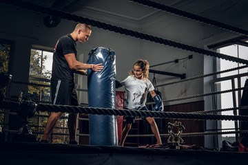 Fototapeta na wymiar Experienced boxer trainer is training new little girl boxer for special competitions using punching bag.