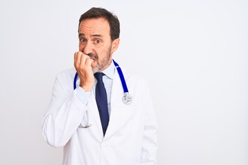 Middle age doctor man wearing coat and stethoscope standing over isolated white background looking stressed and nervous with hands on mouth biting nails. Anxiety problem.