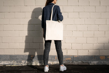 Urban mockup of tote bag. Girl holding white cotton tote bag on a brick wall background. Template...