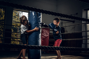 Obraz na płótnie Canvas Dark photo shoot of kids training with big punching bag at boxing studio.
