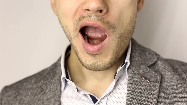 close-up on male chin with three-day stubble. tired business man in gray jacket and white speckled shirt speaks, yawns twice after busy day and smiles. No face, close up on opening mouth