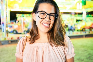Young beautiful woman wearing glasses smiling happy and excited at funfair around lights at night