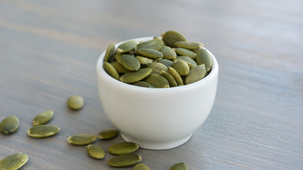 Pumpkin seeds in white bowl over wooden background close up