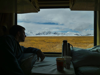 CLOSE UP: Male traveler looks at mountains through the window of overnight train
