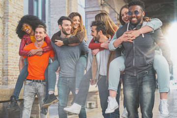 Four multiracial couples having fun piggybacking under the city arcades in the morning. Students having fun in the city..