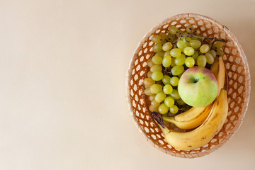 A bunch of green grapes, apple and ripe bananas in a small wicker decorative basket. Seasonal fruits, autumn gifts. Healthy eating. Flat lay, copy space.