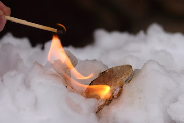 Stone of Calcium carbide (calcium acetylide) burn with big flame in white snow. Piece of carbide react with water from snow and this proces producing gas acetylene.