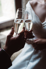 Close up of married couple toasting champagne glasses at wedding party. Hands bride and groom clinking glasses at wedding reception.