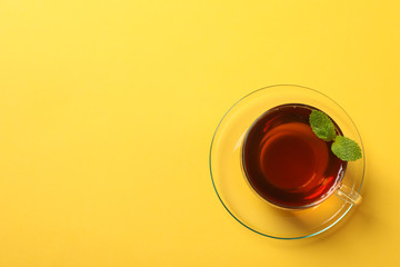Cup of tea and mint leaves on yellow background, space for text
