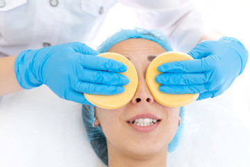 Fototapeta premium close-up hands of beautician makes client facial massage sponges