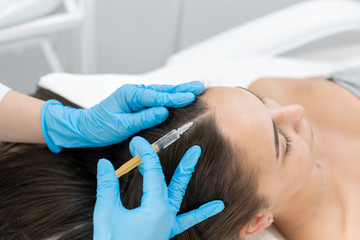 Beautician injections for healthy hair growth. Mesotherapy of the scalp. A young girl is undergoing...