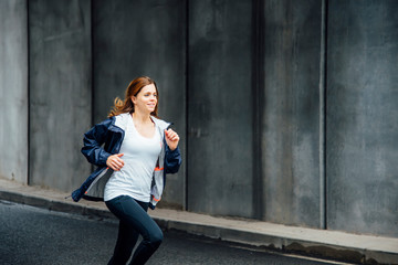 Fototapeta premium Side View Of A Smiling Young Woman Running On The Street. Urban life.