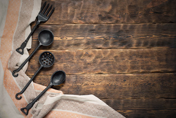 Iron fork, spoon and towel on a brown wooden kitchen table background with copy space.