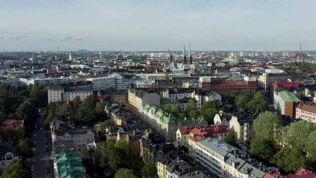 Aerial, tracking, drone shot, overlooking a park, the st johns church and the Eira cityscape, on a sunny, summer day, in Helsinki, Uusimaa, Finland
