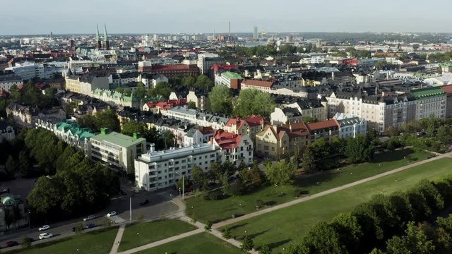 Aerial, flyover, drone shot, over a park and the Eira cityscape, overlooking buildings and the st john church, on a sunny, summer day, in Helsinki, Uusimaa, Finland
