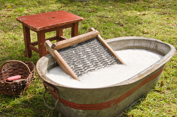An old fashioned washing trougth filled with water, a vintage washboard and soap that wash the laundry
