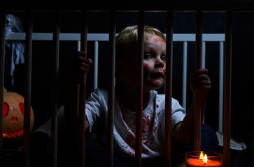 Halloween boy with blood on his face behind bed bars with pumpkin