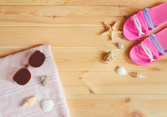 Pink flip flops, sunglasses, towel, starfishes and seashells on wooden background.