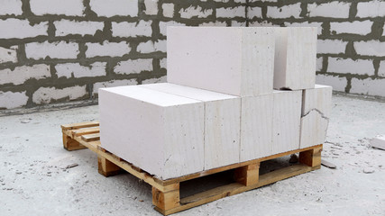 Lightweight concrete blocks on a pallet. Against the background of the walls at a construction site.