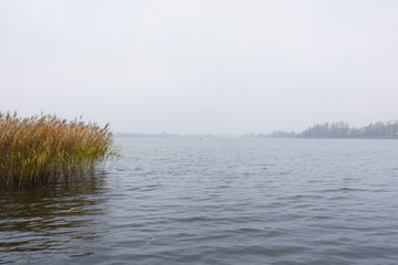 Landscape with a lake during the fog mist; plants water boats fishing view, beautiful sky clouds calm leisure reeds