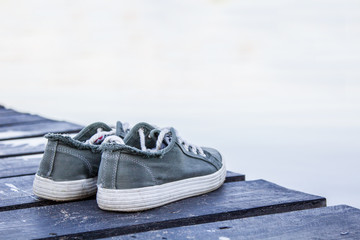 gray sneakers are on a wooden pier near the water. Closeup