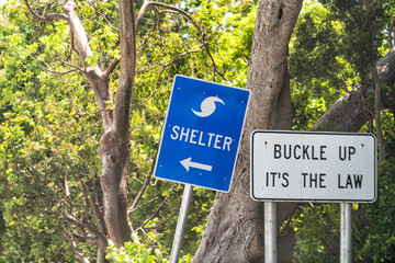 Hurricane evacuation shelter blue sign on road and seat belt buckle up it's the law text with arrow direction in Naples, Florida coast during day