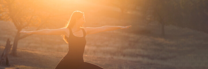 Young healthy woman practicing yoga at sunset on the beautiful autumn hills in the park.