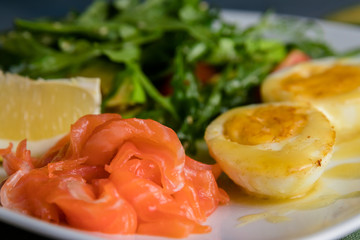 Salad with salted trout, avocado, arugula and fried egg in butter. Close up on the grey background