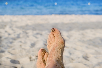 Girl sits near the sea. A woman lying on a chaise longue near the sea. Feet girl on the beach near the water, close-up.