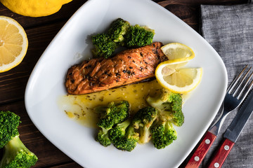 Grilled trout steak on a white plate with broccoli and lime. Cutlery on the wooden background