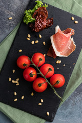 Prosciutto, cherry tomatoes and pine nuts. Fresh appetizer on the black board