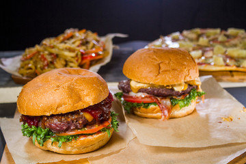 Order in a fast food restaurant. Two meat burgers with vegetables, udon noodles and pizza on the table.