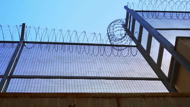 high prison fence with barbed wire, bottom view. Prison fence against clear sky.