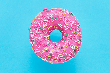 Sprinkled Pink Donut. Glazed sprinkled donut on blue background. Top view, copy space