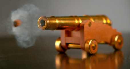 MACRO, DOF: Vintage brass toy cannon shoots a small cannonball across the room.