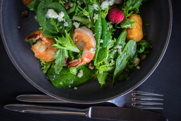 Closeup view on Tiger prawn salad with brie cheese, raspberries, walnut. Wooden board on gray background
