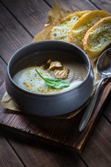 Cappuccino soup with mushrooms on wooden cutting board. Three slices of white bread and a spoon on the brown wooden background in restaurant. Vertical photo.