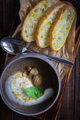 Cappuccino soup with mushrooms on wooden cutting board. Three slices of white bread and a spoon on the brown wooden background in restaurant. Vertical photo.