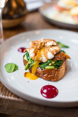Poached egg with smoked eel and sauteed spinach on brioche toast. Close up view.