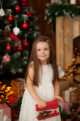 Happy pretty girl 4-5 playing with a toy railway in front of a Christmas tree with Christmas presents. New Year holiday.