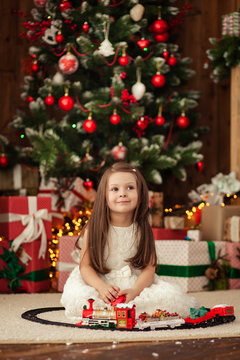 Happy pretty girl 4-5 playing with a toy railway in front of a Christmas tree with Christmas presents. New Year holiday.