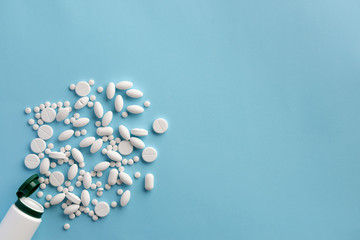 Bottle with scattered pills on blue background. Flat lay.