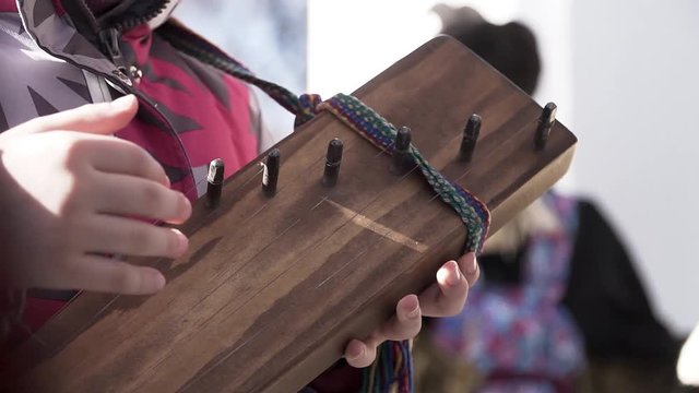 Close up for hands of a little child trying too play the traditional stringed instrument. Clip. A girl playing unusual music instrument outside.