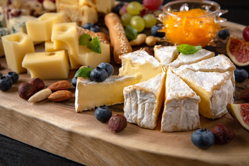 Wooden board with different types of cheese, nuts, berries and fruits.
