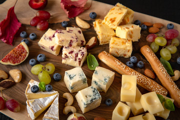 Wooden board with different types of cheese, nuts, berries and fruits.